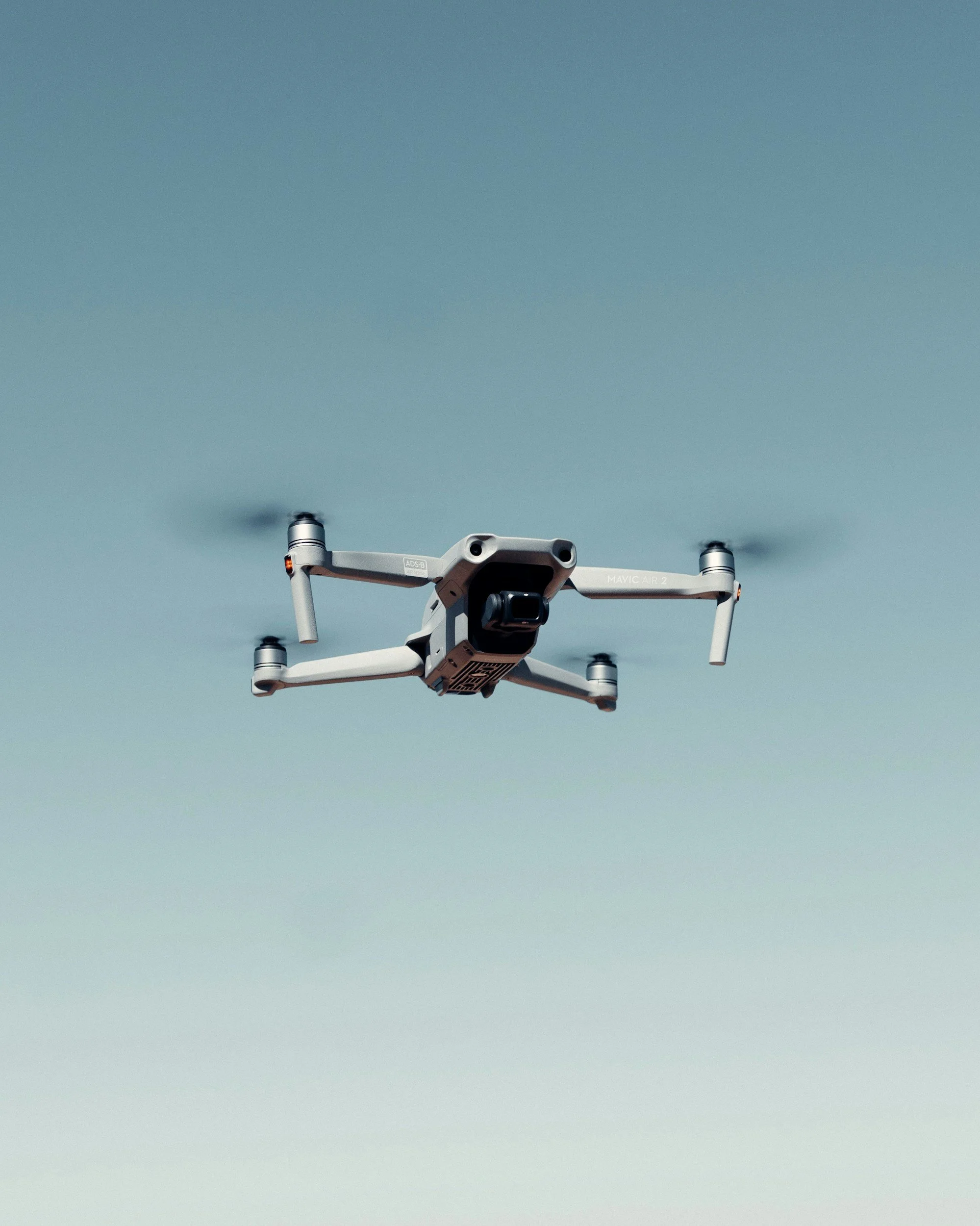 A drone flying in the sky against a clear blue background.