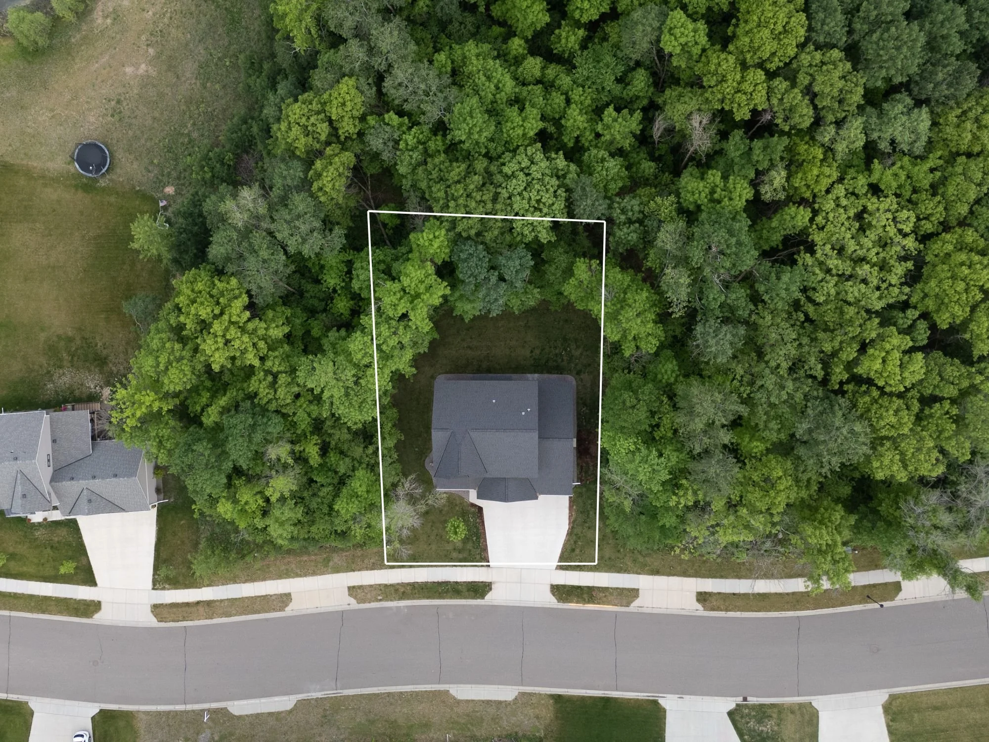 An aerial view of a suburban neighborhood showing a house outlined in white, surrounded by trees and a sidewalk in front.