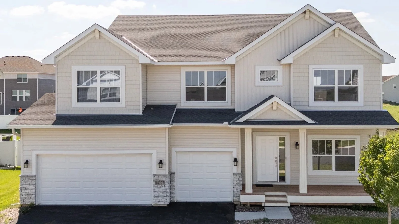 Front view of a two-story suburban house with white siding, a dark shingled roof, double garage doors, and a small front porch with stairs.