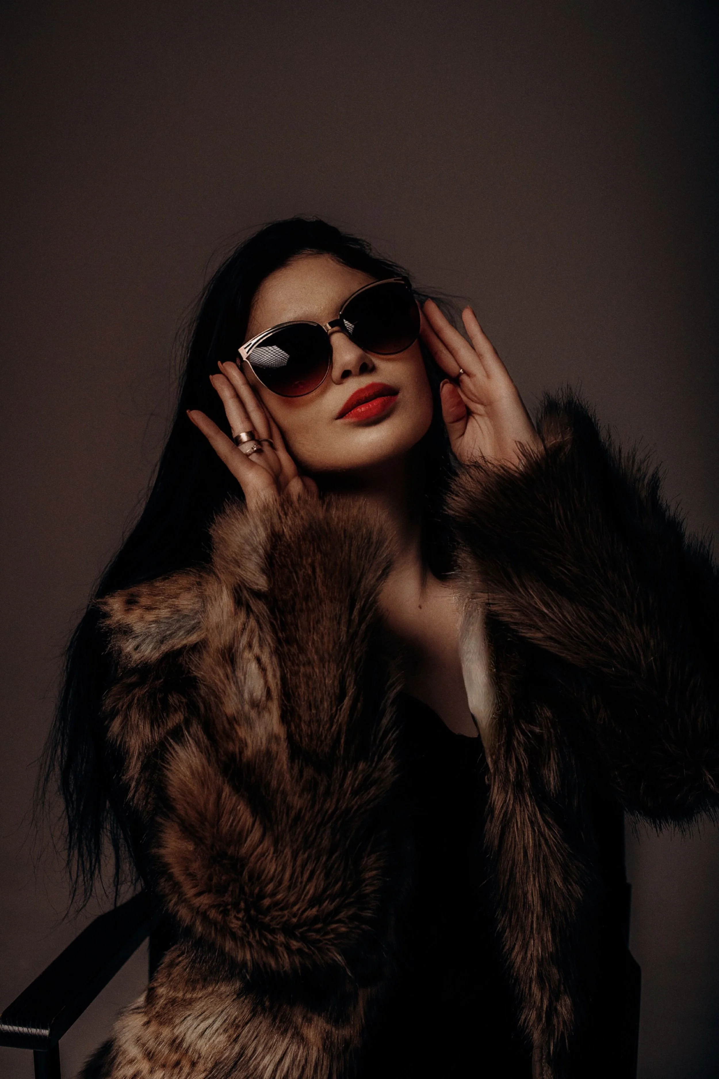 A woman wearing oversized sunglasses, red lipstick, and a faux fur coat, posing.