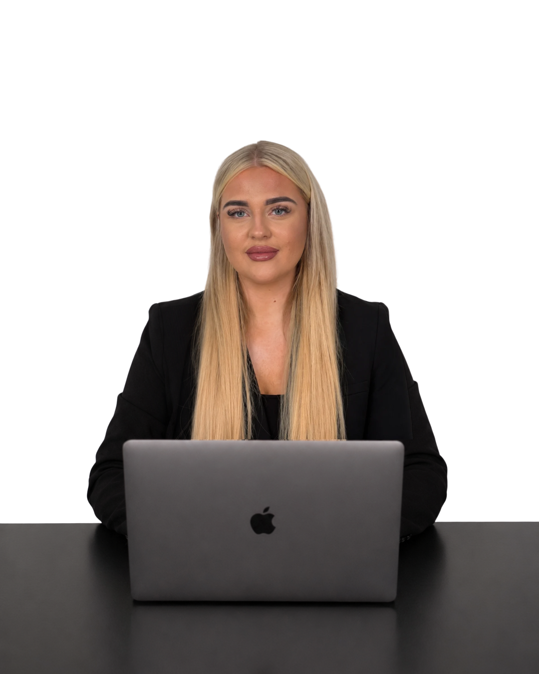 A woman with long blonde hair and a black blazer sitting at a black table with a silver MacBook.