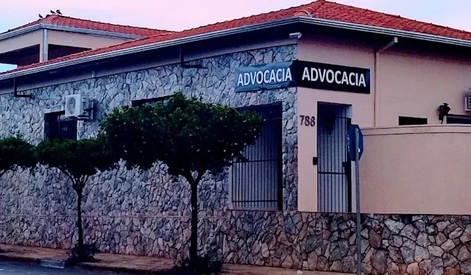 Edifício com sinal de advocacia na fachada, parede de pedra, árvores na calçada e postes de trânsito.