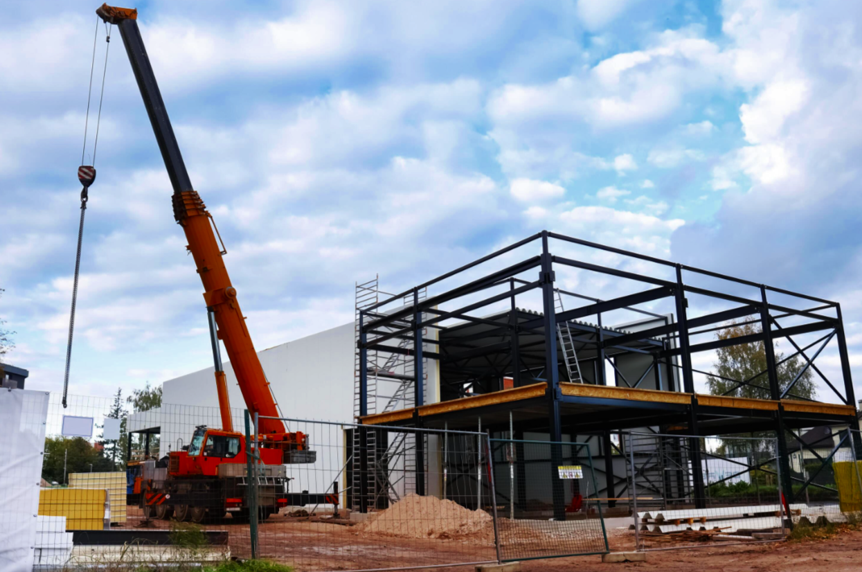 Construction site with a red crane lifting materials and a steel framework building under construction, with scaffolding and ladders.