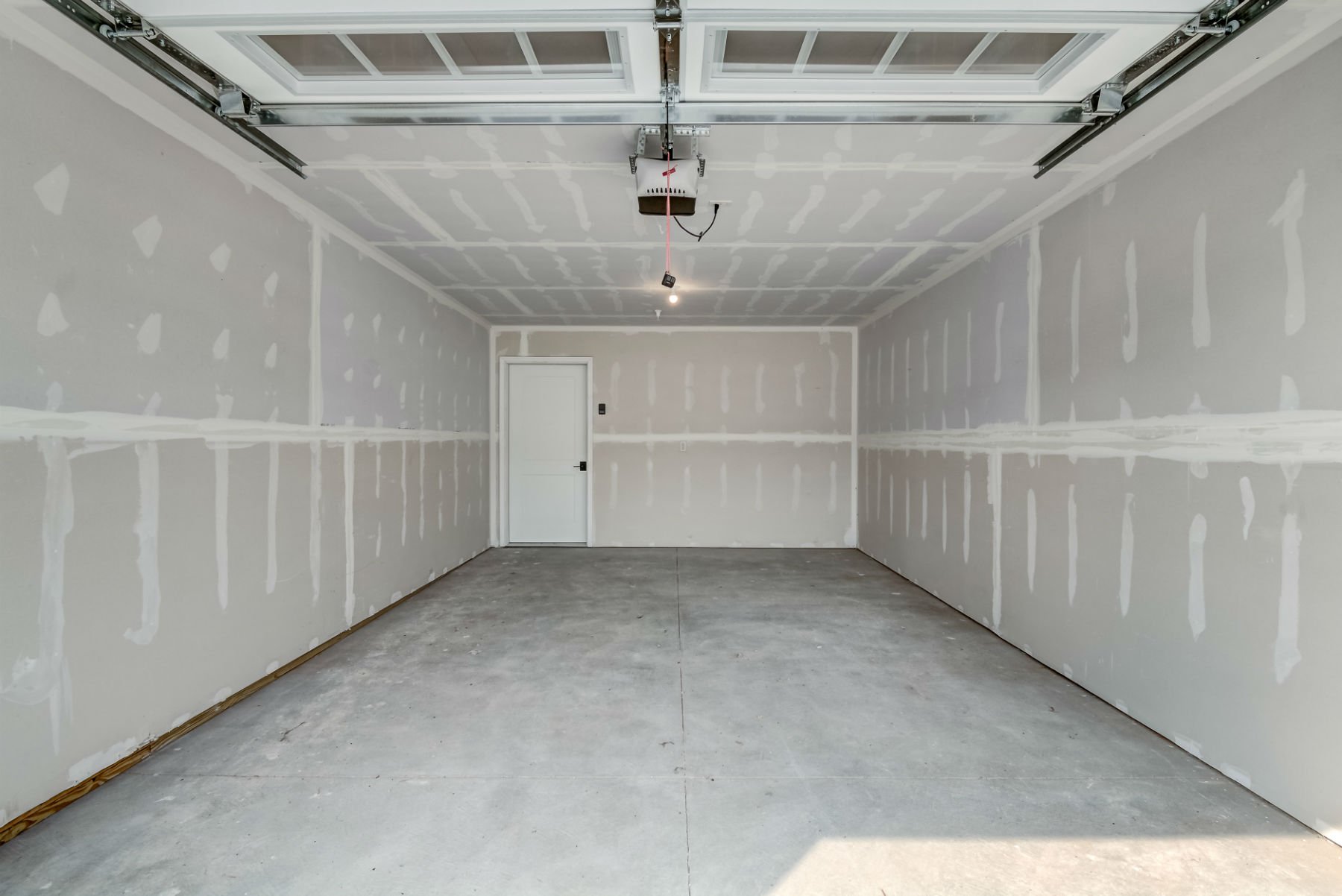 Empty unfinished two-car garage with drywall installed, but no paint or flooring yet, and an open garage door.