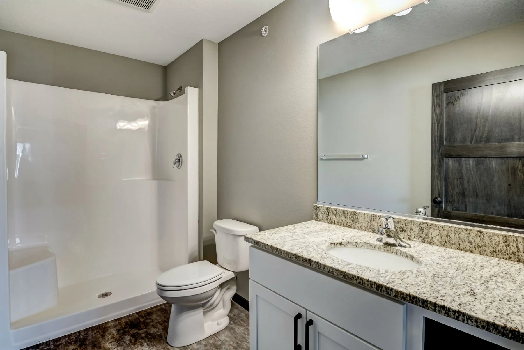 Bathroom with a shower, toilet, granite countertop sink, large mirror, and wooden door.