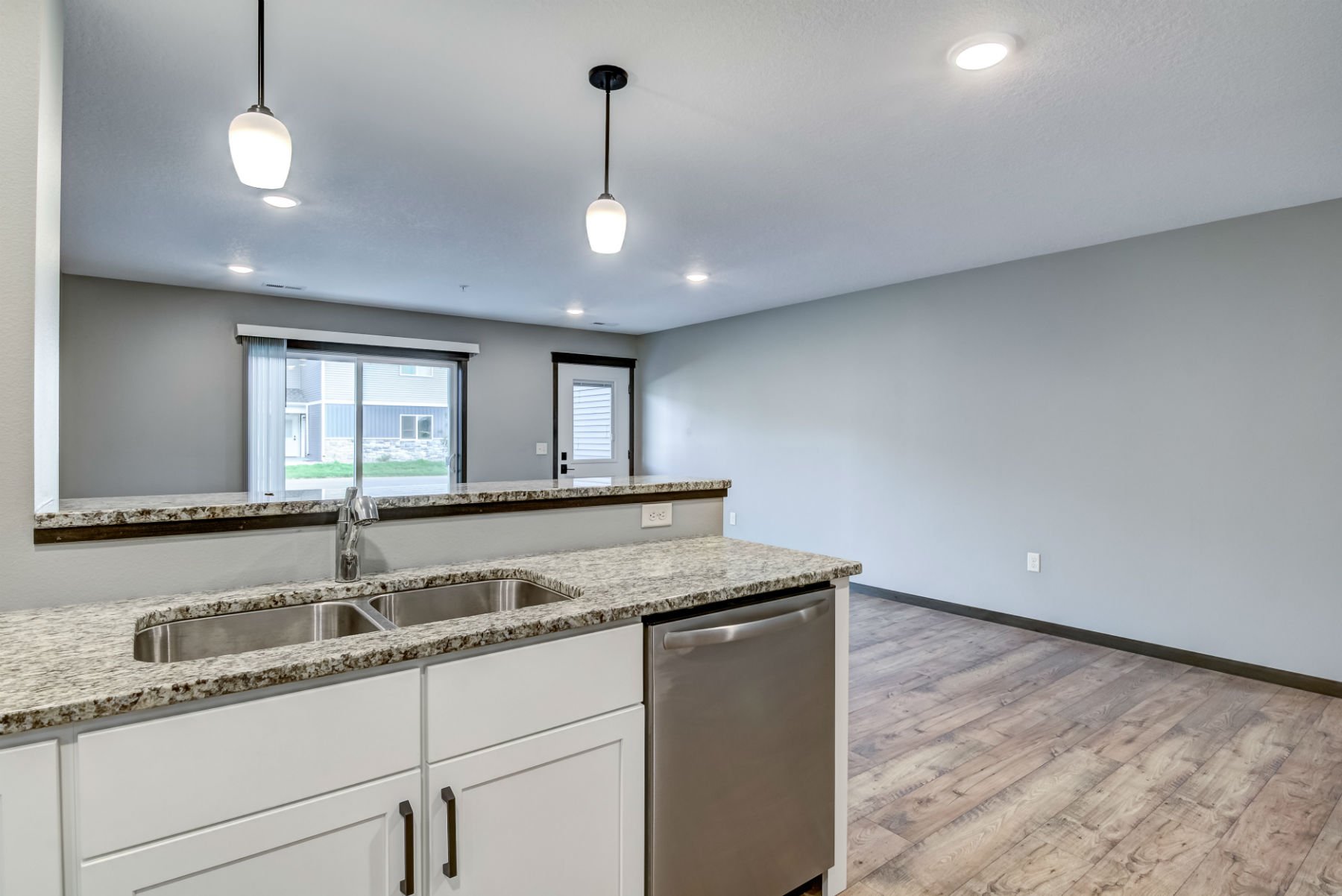 Modern open-concept kitchen with granite countertops, white cabinetry, stainless steel appliances, and a view into a living area with large windows and wood flooring.