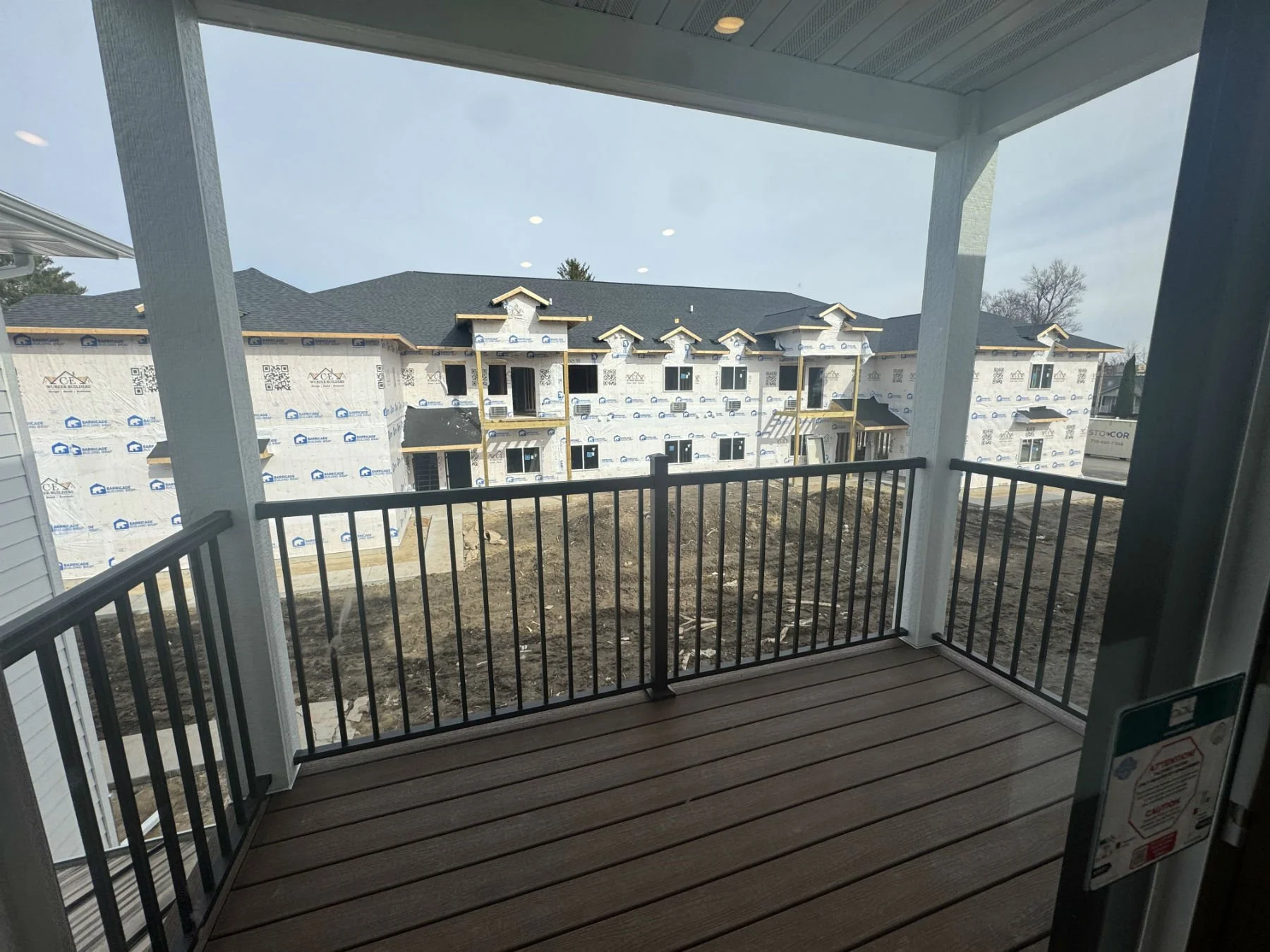 View from a balcony overlooking a construction site of a new apartment building with unfinished walls and missing siding.