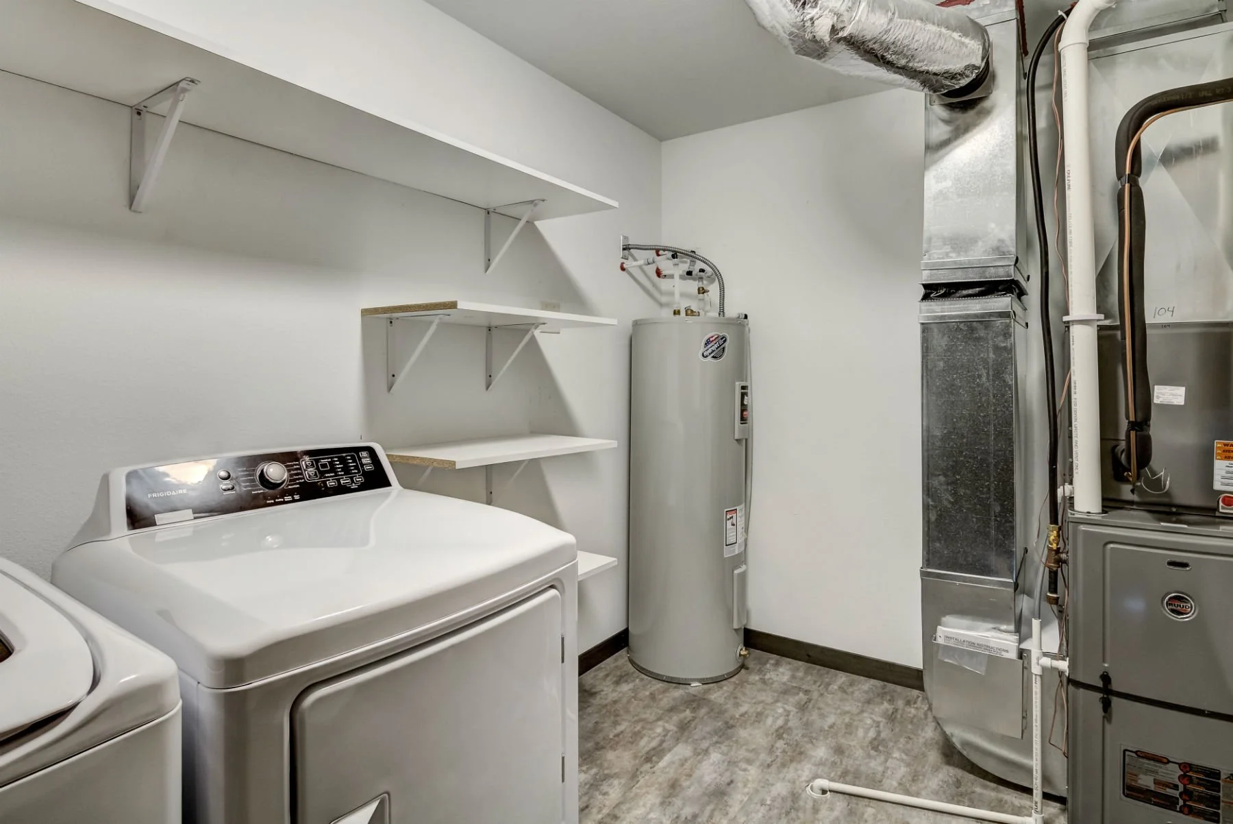 Laundry room with white washer and dryer, white water heater, shelves on wall, and HVAC system.
