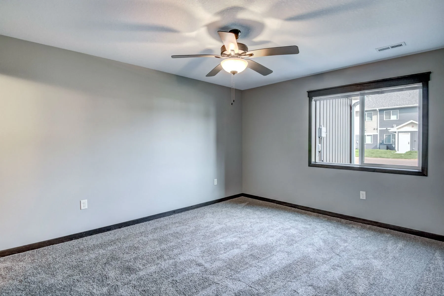 Empty room with light gray walls, a ceiling fan, a large window, and a gray carpeted floor.