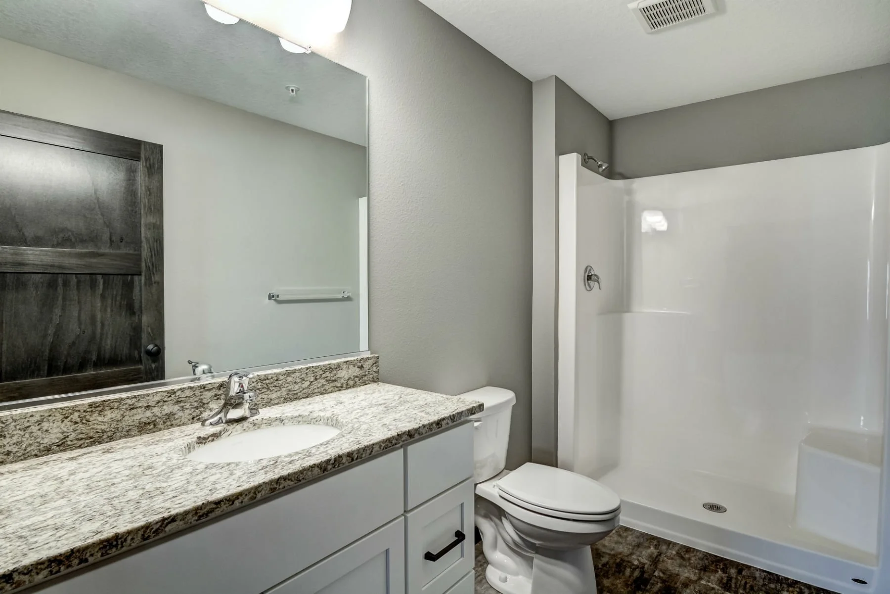 Bathroom with granite countertop, white vanity, mirror, toilet, and shower with white walls and gray ceiling.