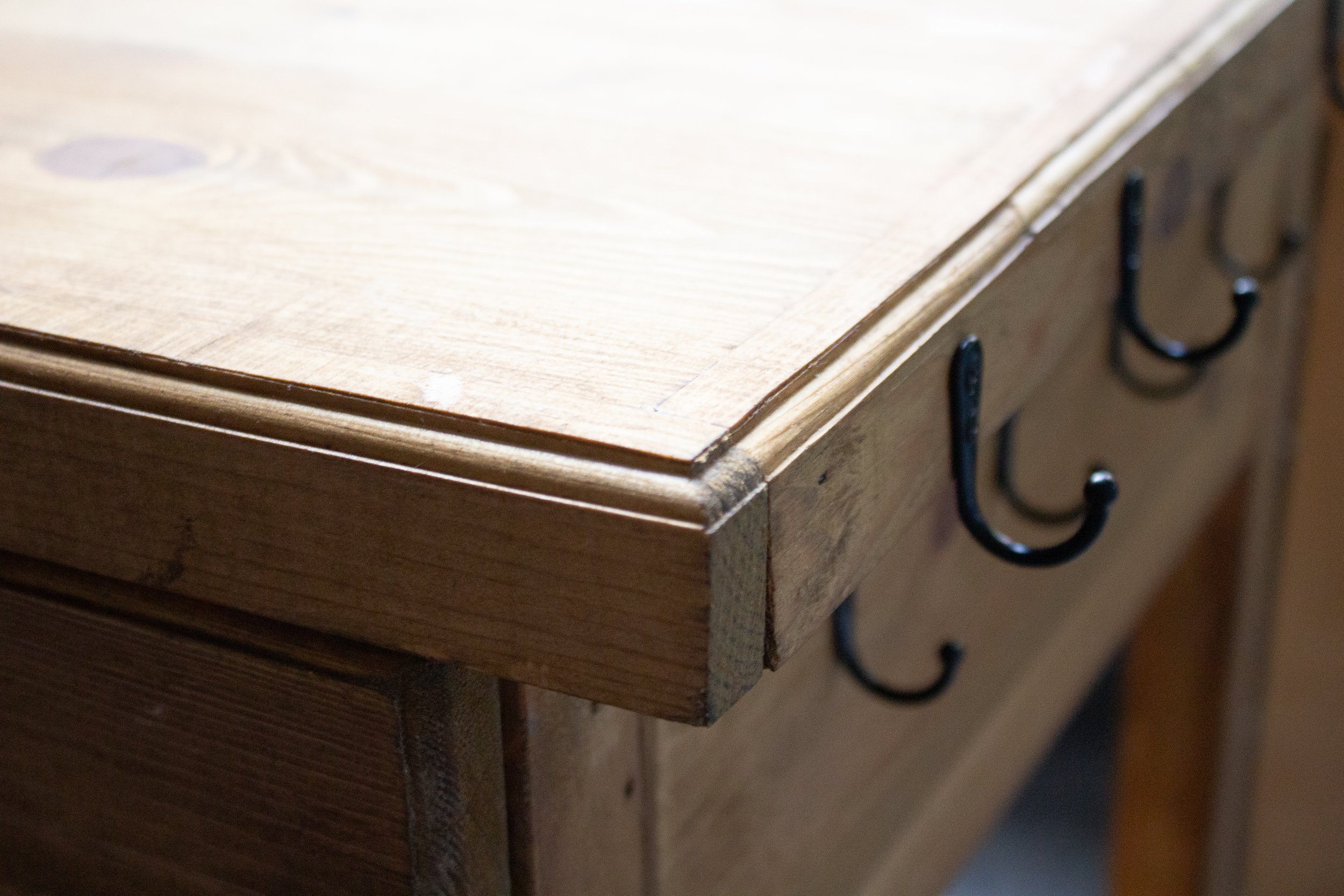 Close-up of a wooden dresser with black metal handles, showing the top and side edge.