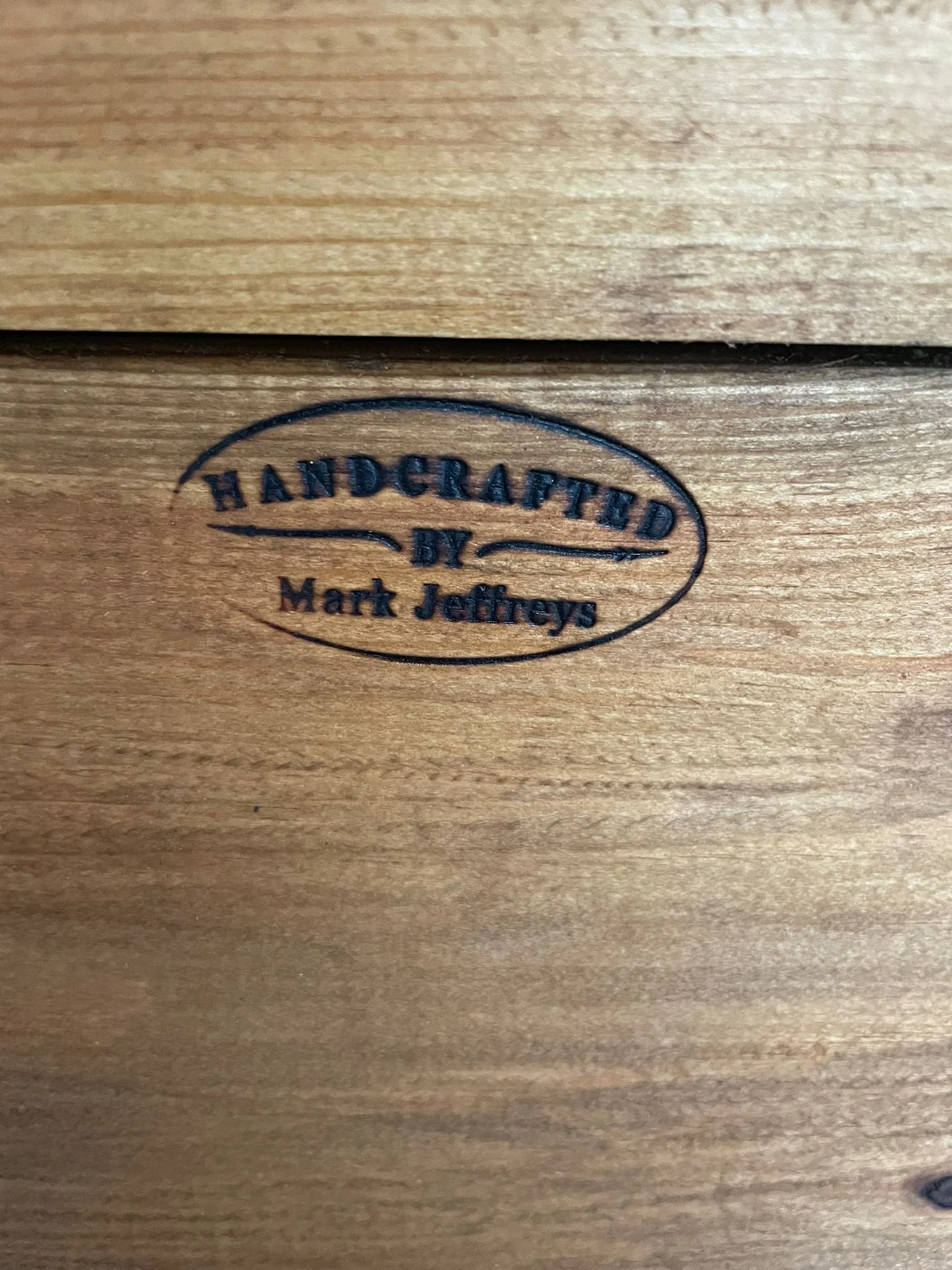 Close-up of a wooden surface with a branding stamp reading 'HANDCRAFTED BY Mark Jeffreys'.