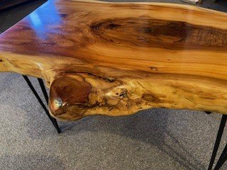 Close-up of a wooden table with natural edge and black metal legs.