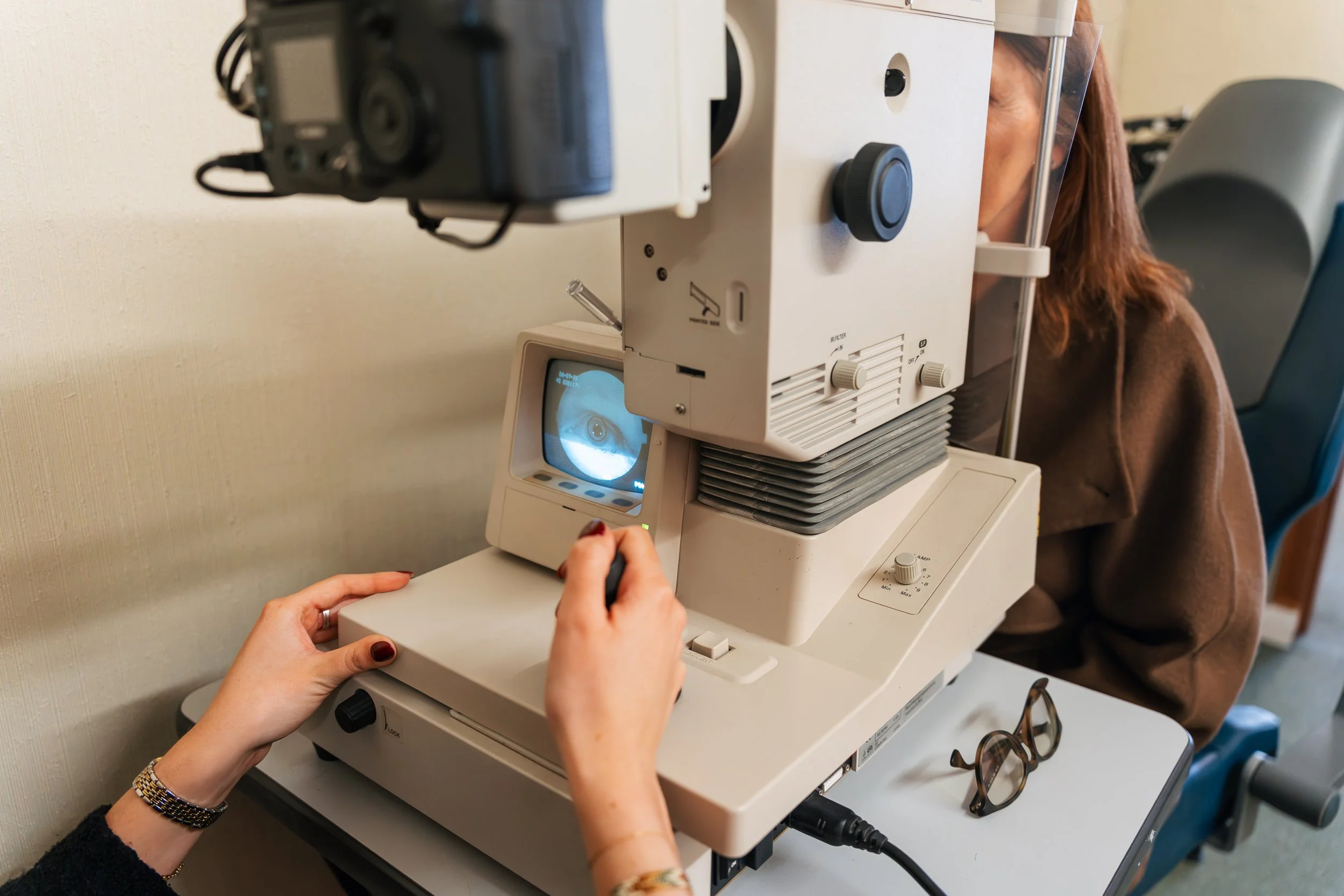 Person looking into an eye examination machine at an eye clinic, with eyeglasses on the table nearby.