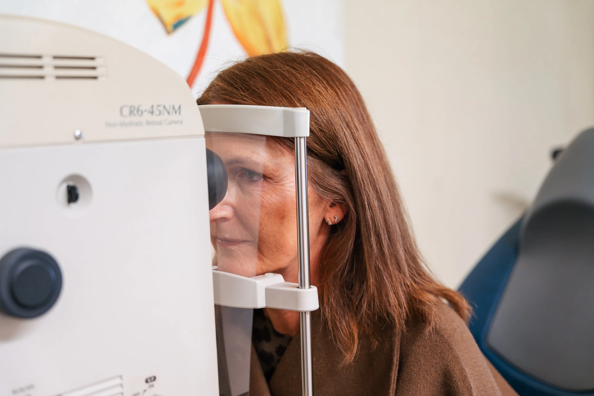 Woman looking through an eye examination machine during an eye test in a clinical setting.