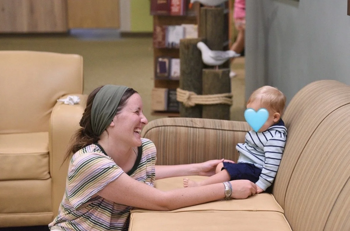 A woman and a young child sitting on the floor, smiling and laughing together in a cozy indoor setting.