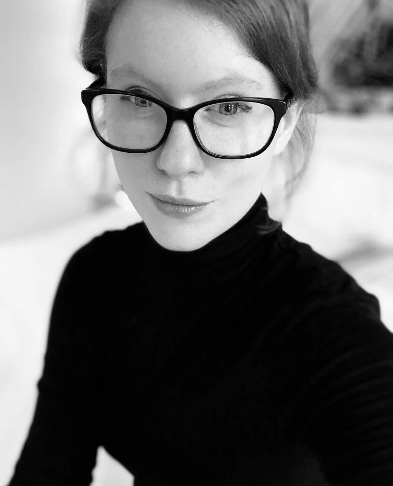 A black and white image of writer and author A.V. Hill. She is wearing a black turtleneck and her trademark black rimmed glasses.
