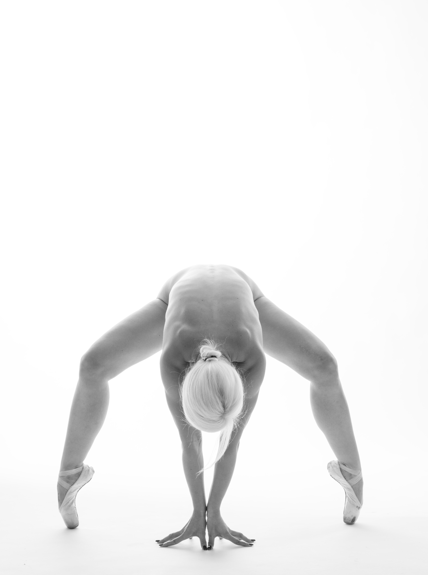 Balletttänzerin in einer handstandähnlichen Pose, ihre Füße in Ballettschläppchen, mit einem dunklen Hintergrund.