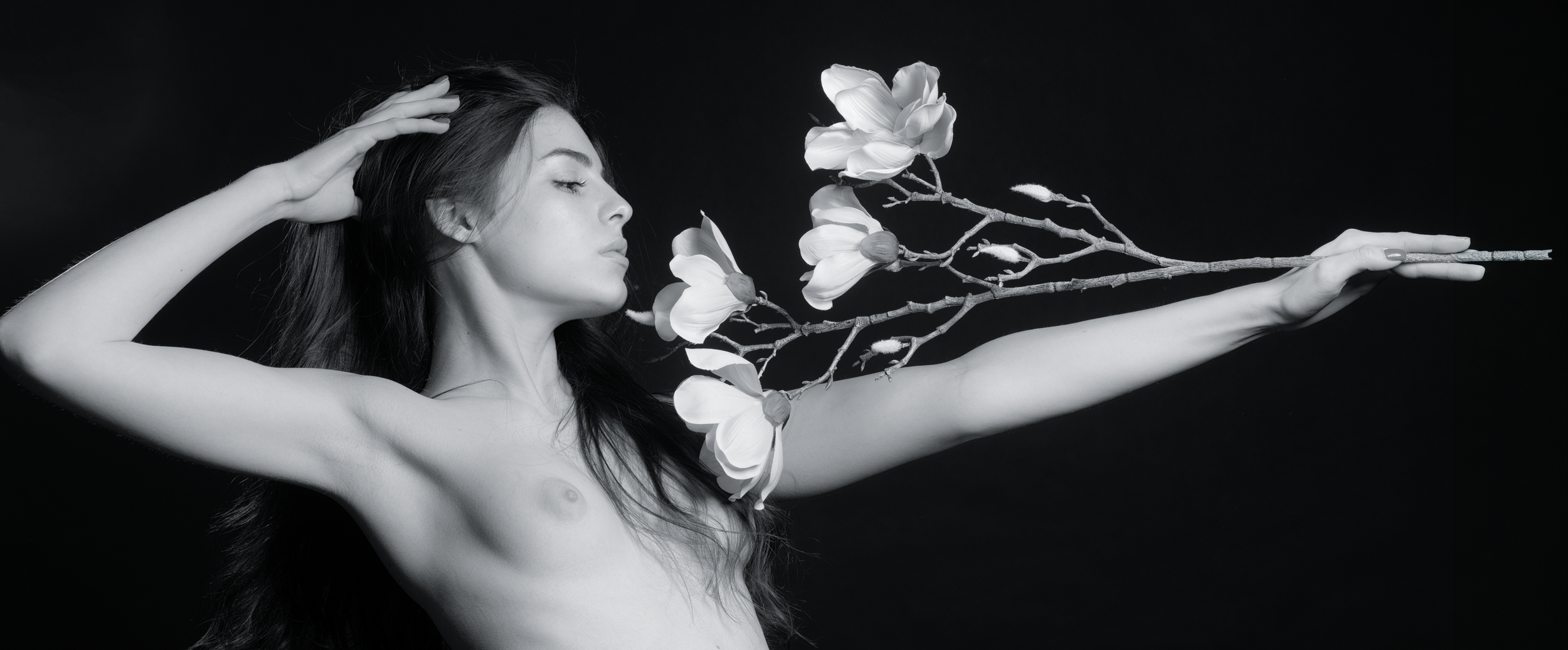 Schwarz-weiß-Bild einer nackten Frau, deren Arm eine Blumenäste mit großen Blüten hält.