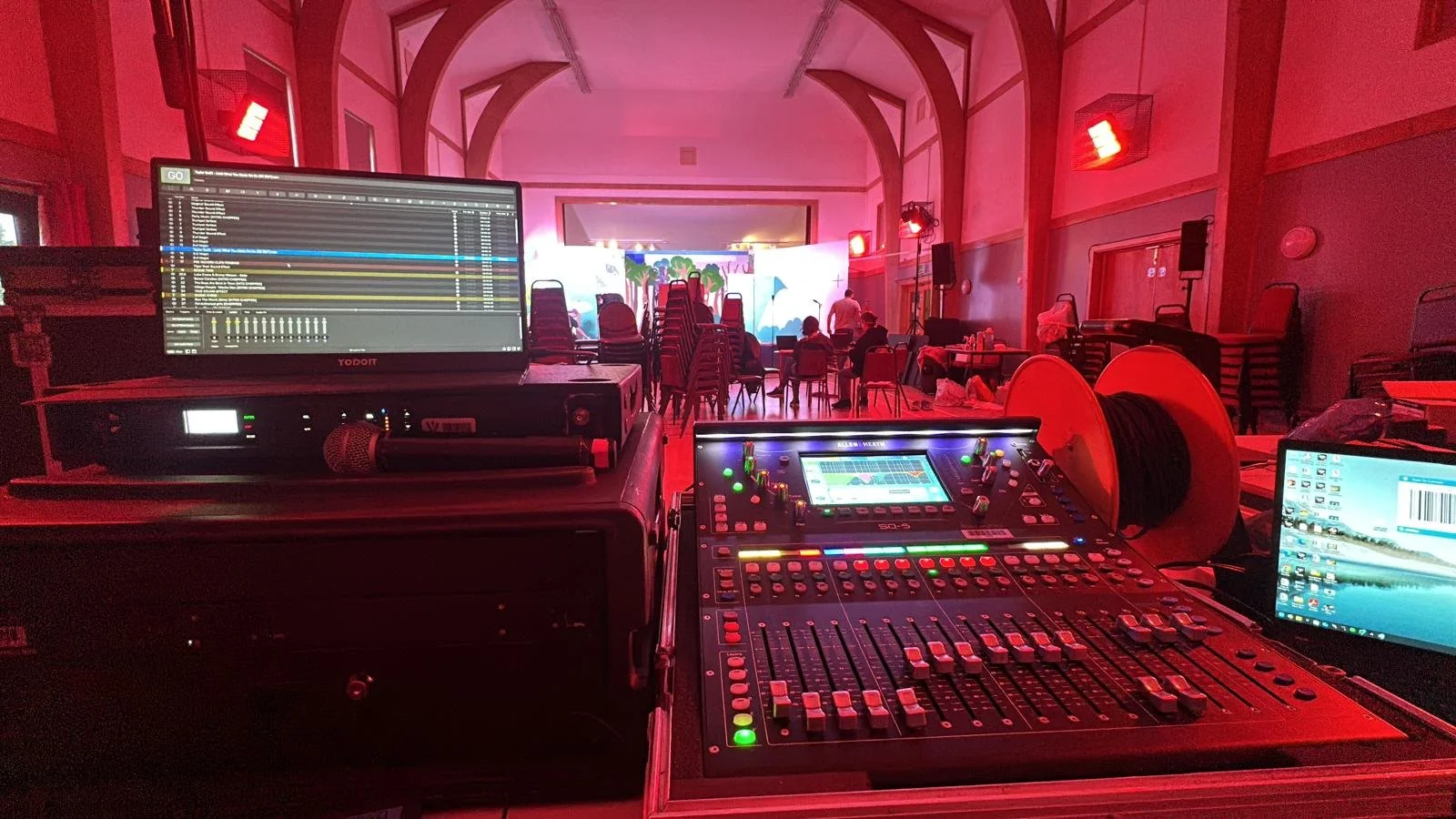 Sound and lighting equipment setup in a dimly lit event hall with chairs and a stage at the front