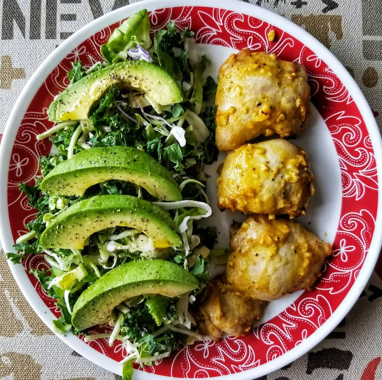 A plate with three chicken pieces covered in yellow sauce and a side salad consisting of mixed greens, avocado slices, and cucumber slices.