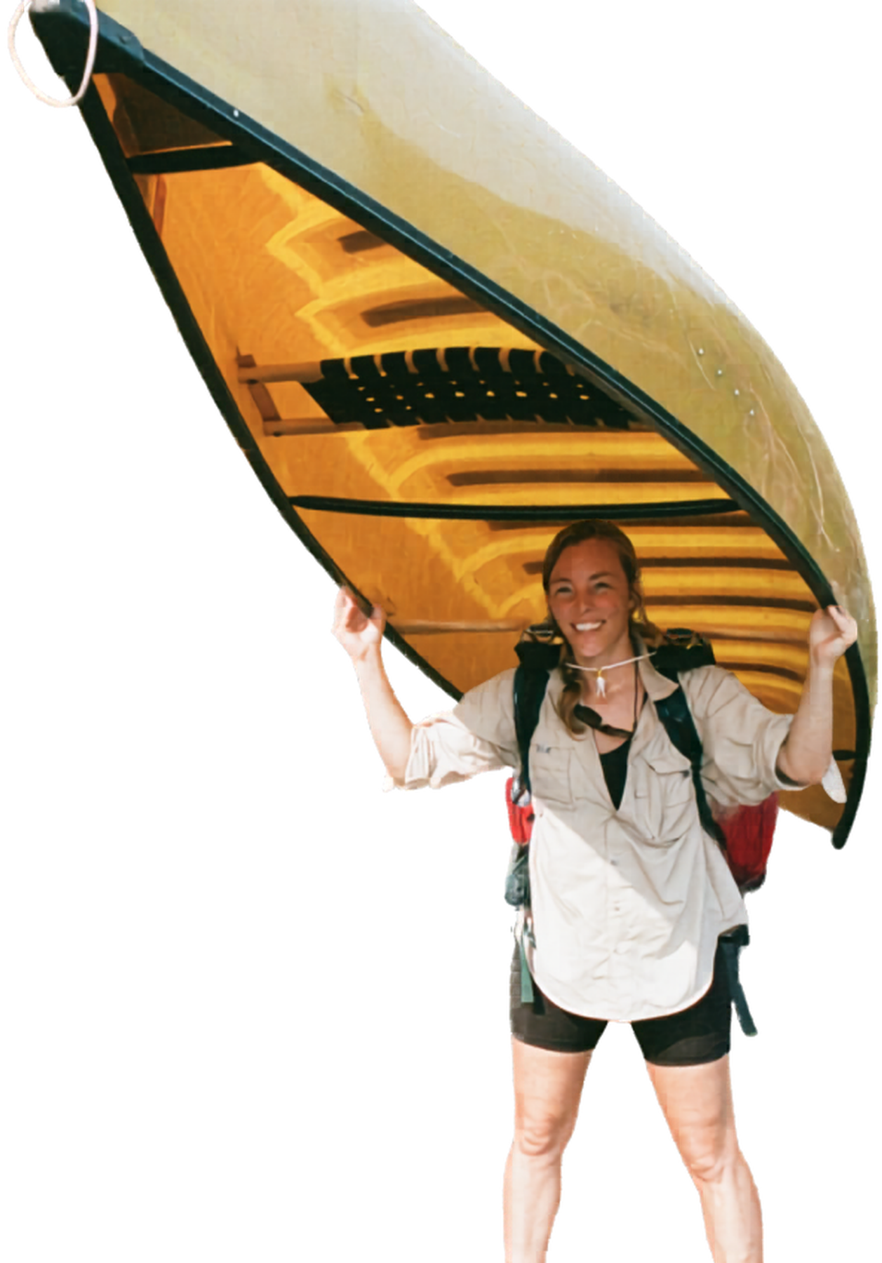 A woman smiling and holding a kayak above her head, wearing a beige shirt, black shorts, and a backpack.