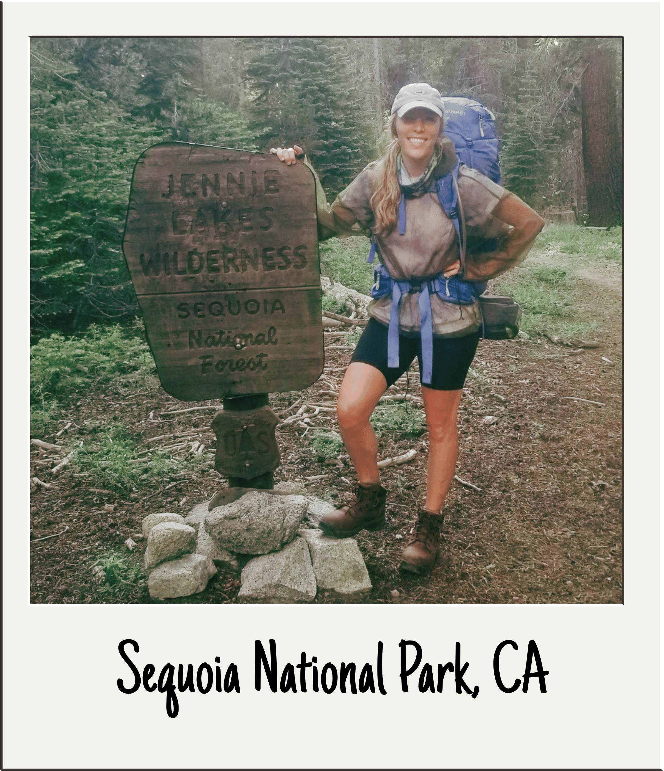 A woman wearing hiking gear, including a cap, backpack, and boots, stands outdoors in a forested area next to a sign for Sequoia National Park in California. She is smiling and posing with her hand on her hip, next to a wooden sign with the park's name and logo.