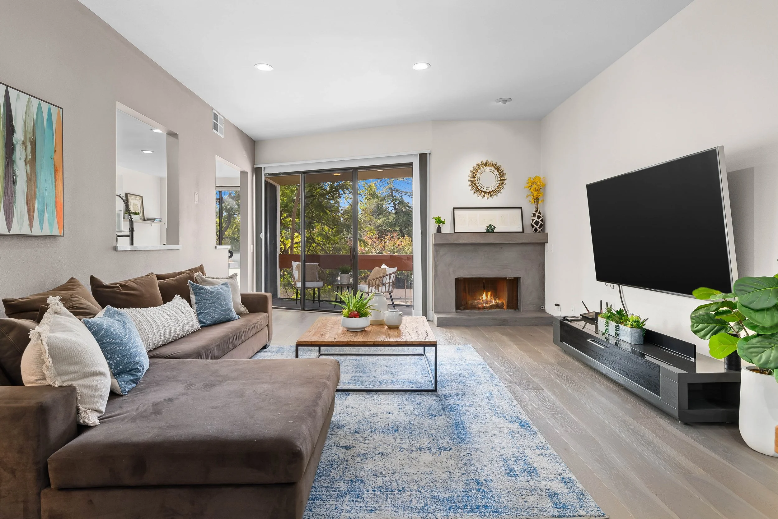 Living room with brown sofa, decorative pillows, fireplace, and large sliding glass doors showing trees outside.