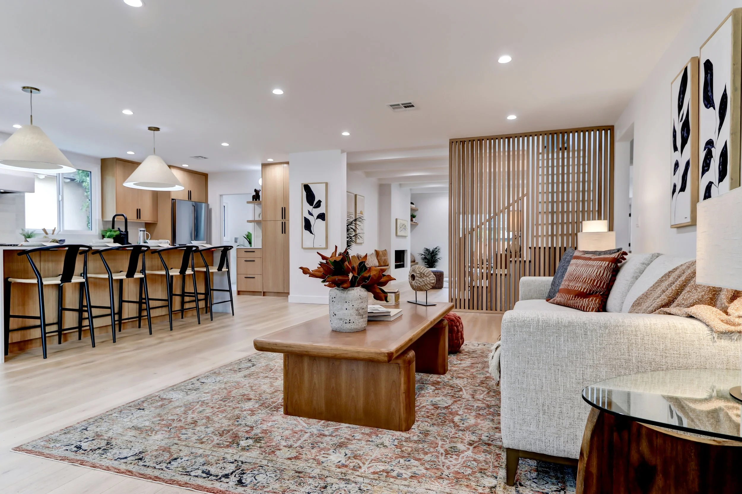 Open-concept living room and kitchen with modern decor, wooden accents, abstract wall art, and a patterned rug.