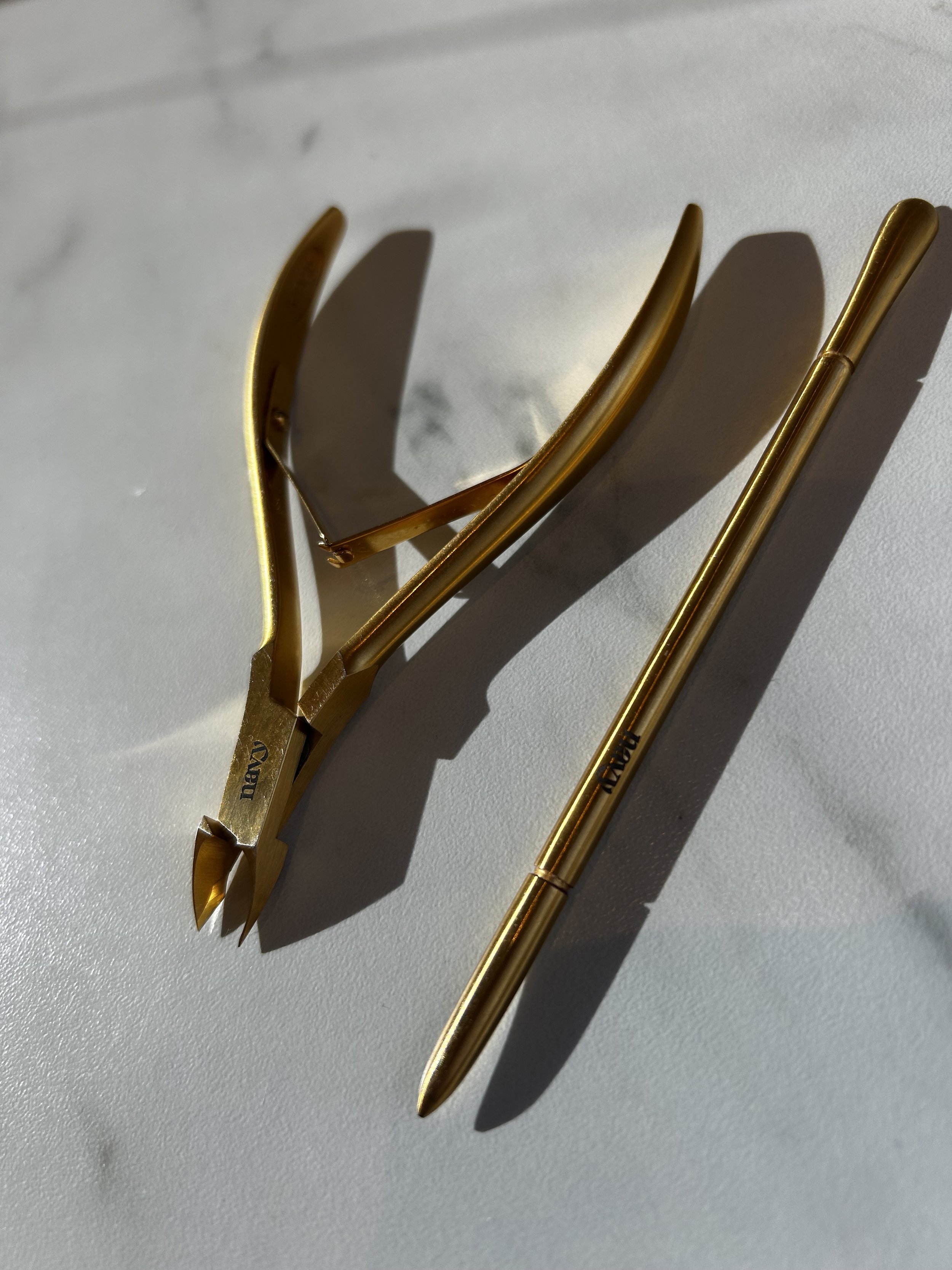A gold-colored hairpin with a curved top shape and a matching gold pen on a white surface with shadows.