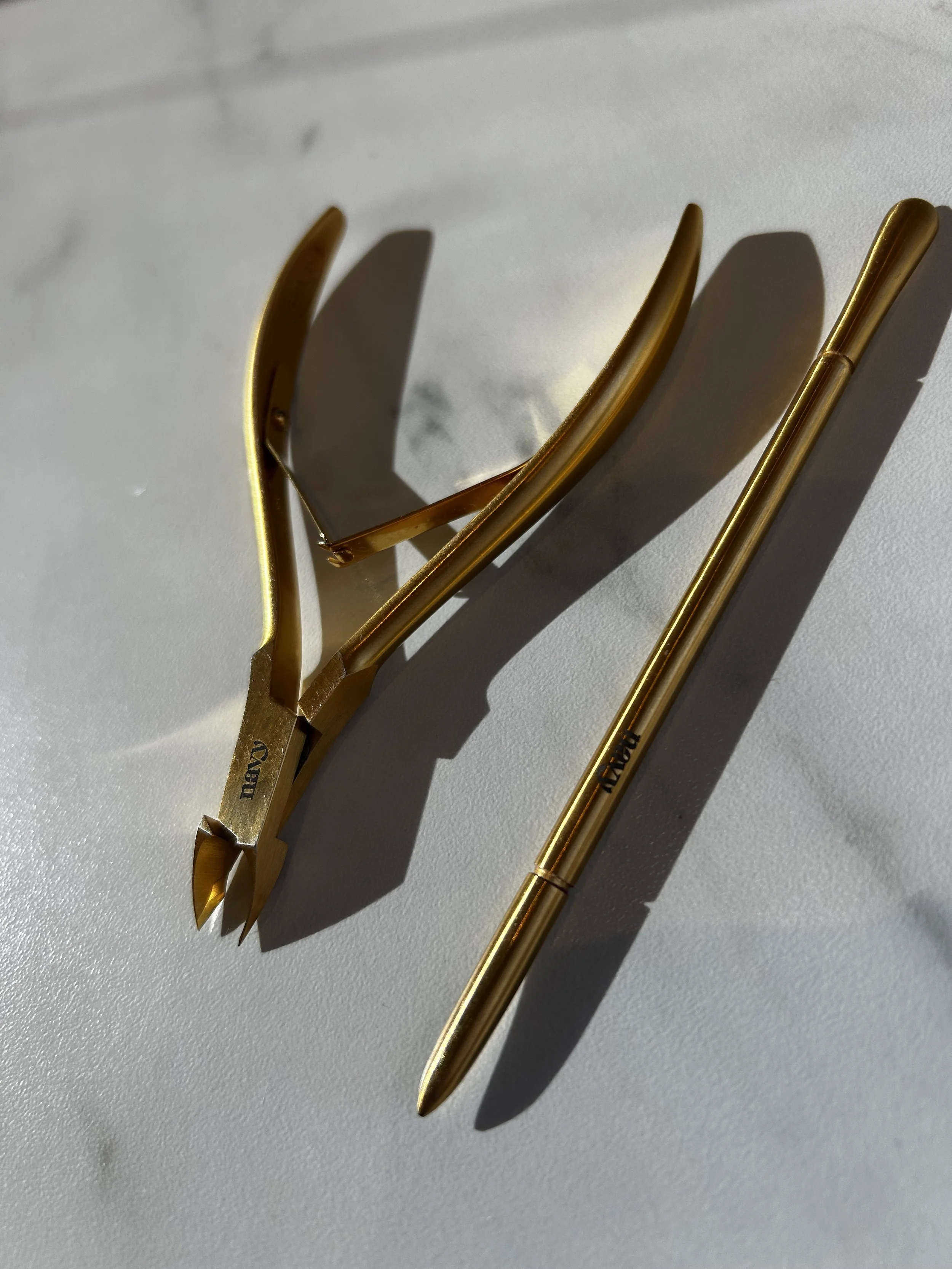 A pair of gold hairpins and a gold pen cast shadows on a white surface.