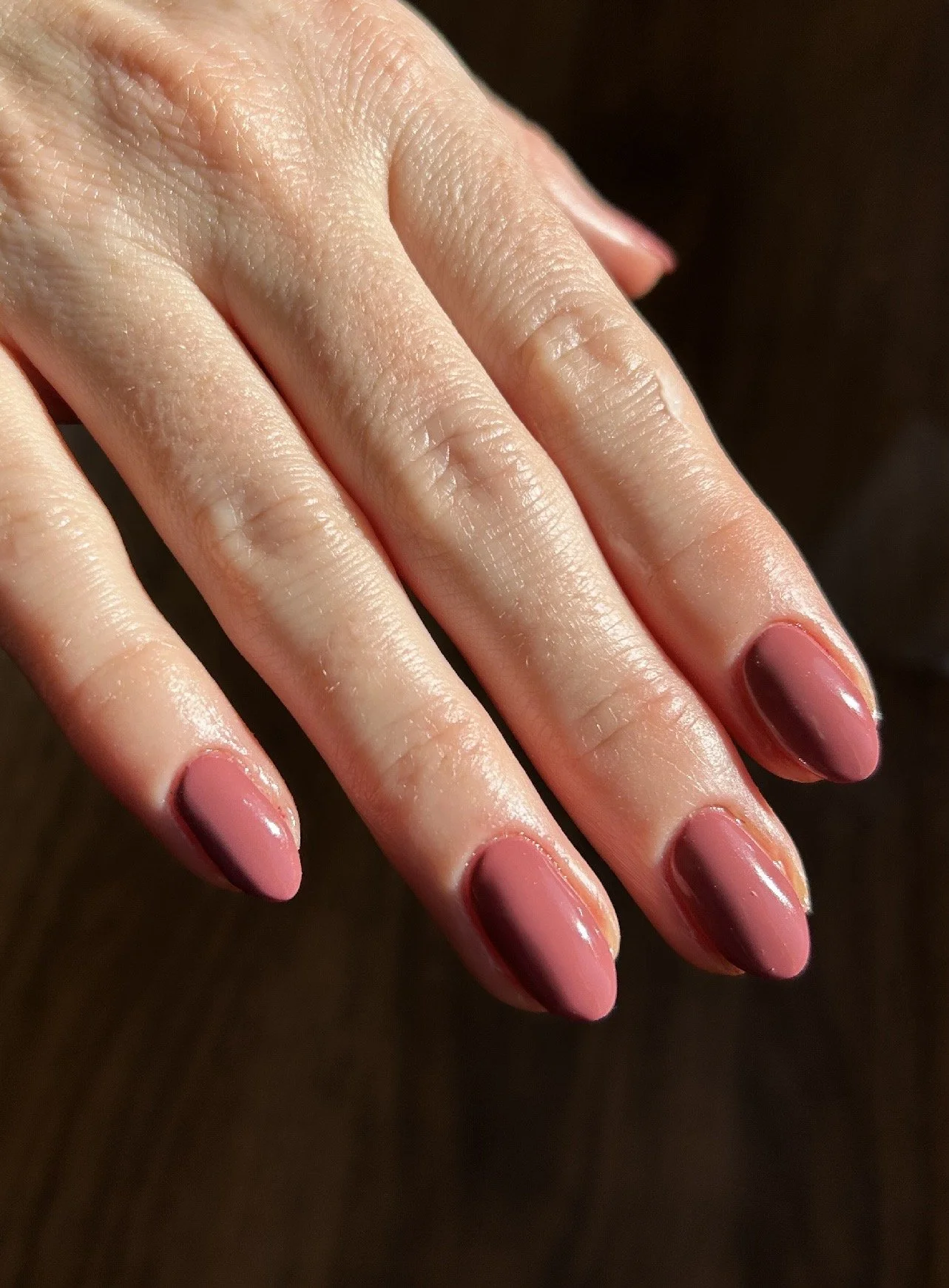 Close-up of a hand with manicured nails painted in shades of pink and red, against a dark background.