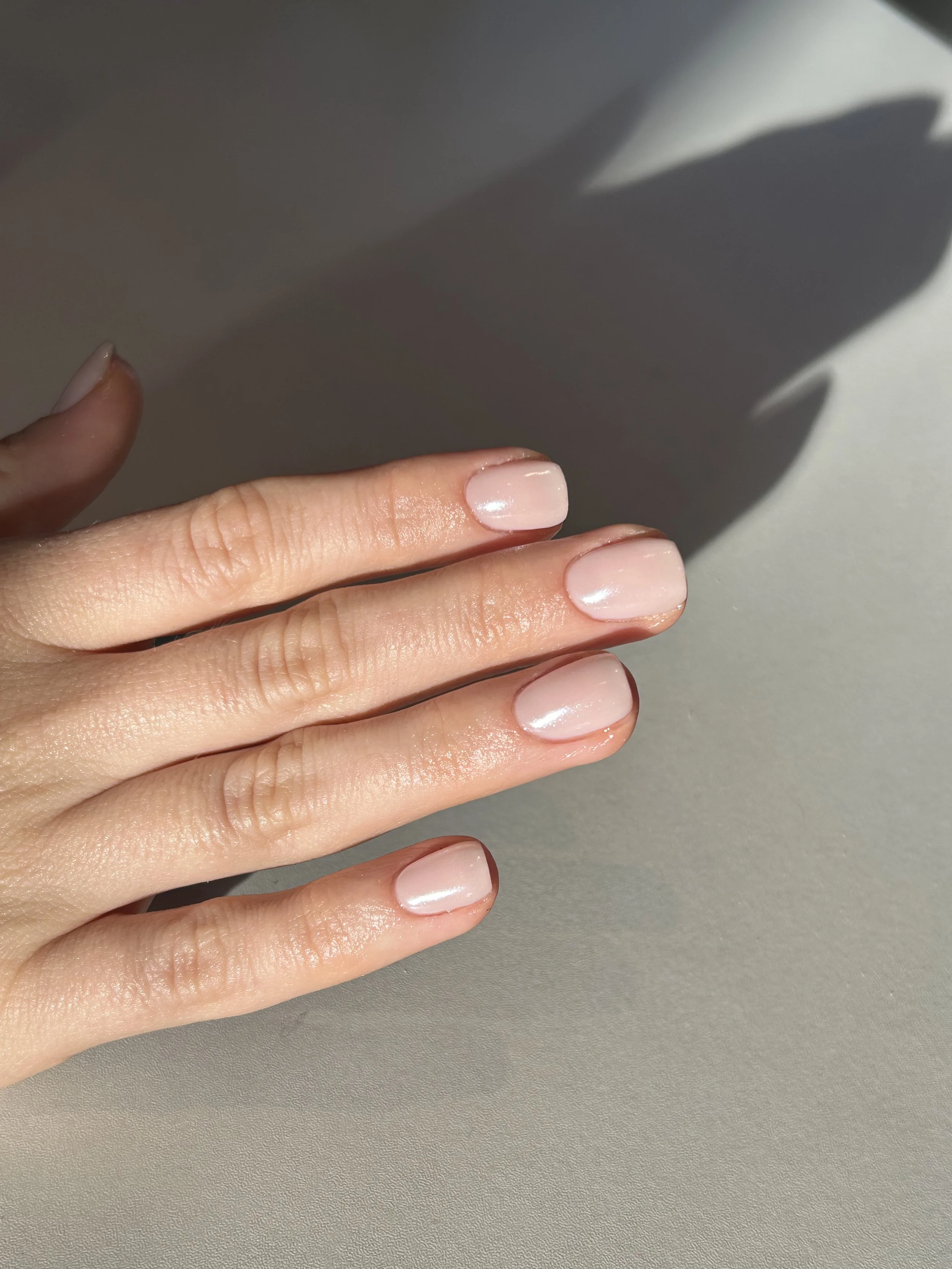 Close-up of a hand with well-manicured, natural-colored nails on a gray surface, casting a shadow.