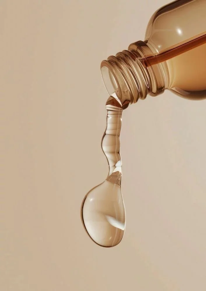 Close-up of a beige-colored bottle tilted and pouring out a clear liquid, with a beige background.