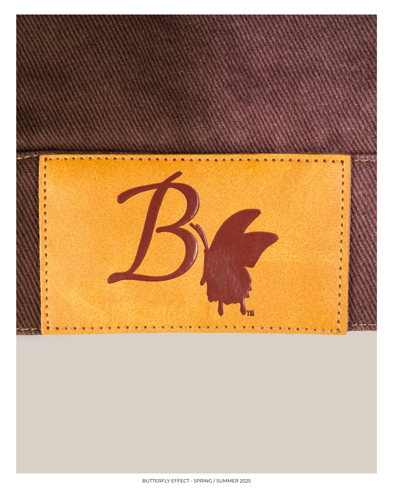 Close-up of a clothing tag with the Bby logo and a butterfly silhouette, attached to a brown fabric material.