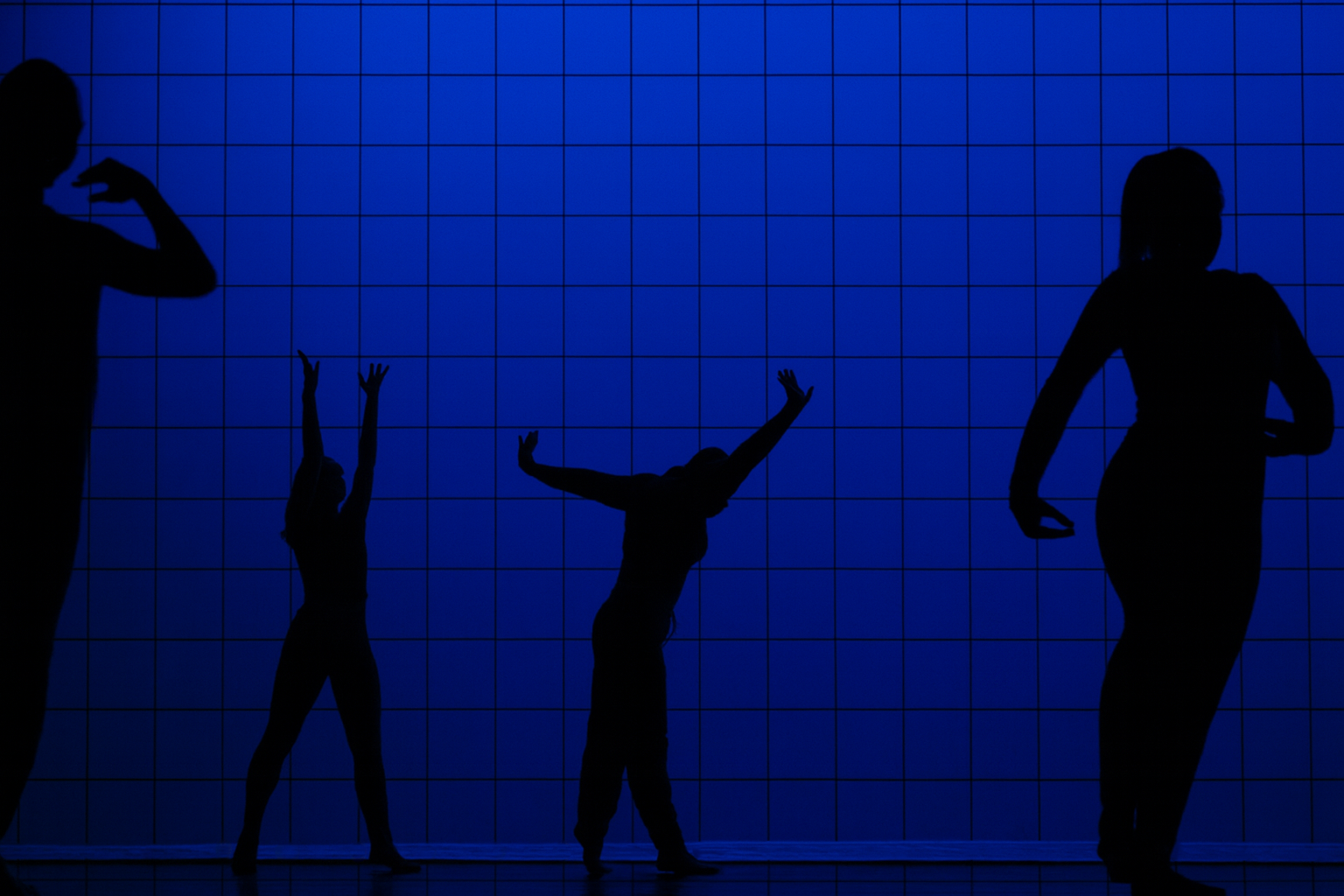 Silhouettes of four people dancing or performing in front of a blue grid background.