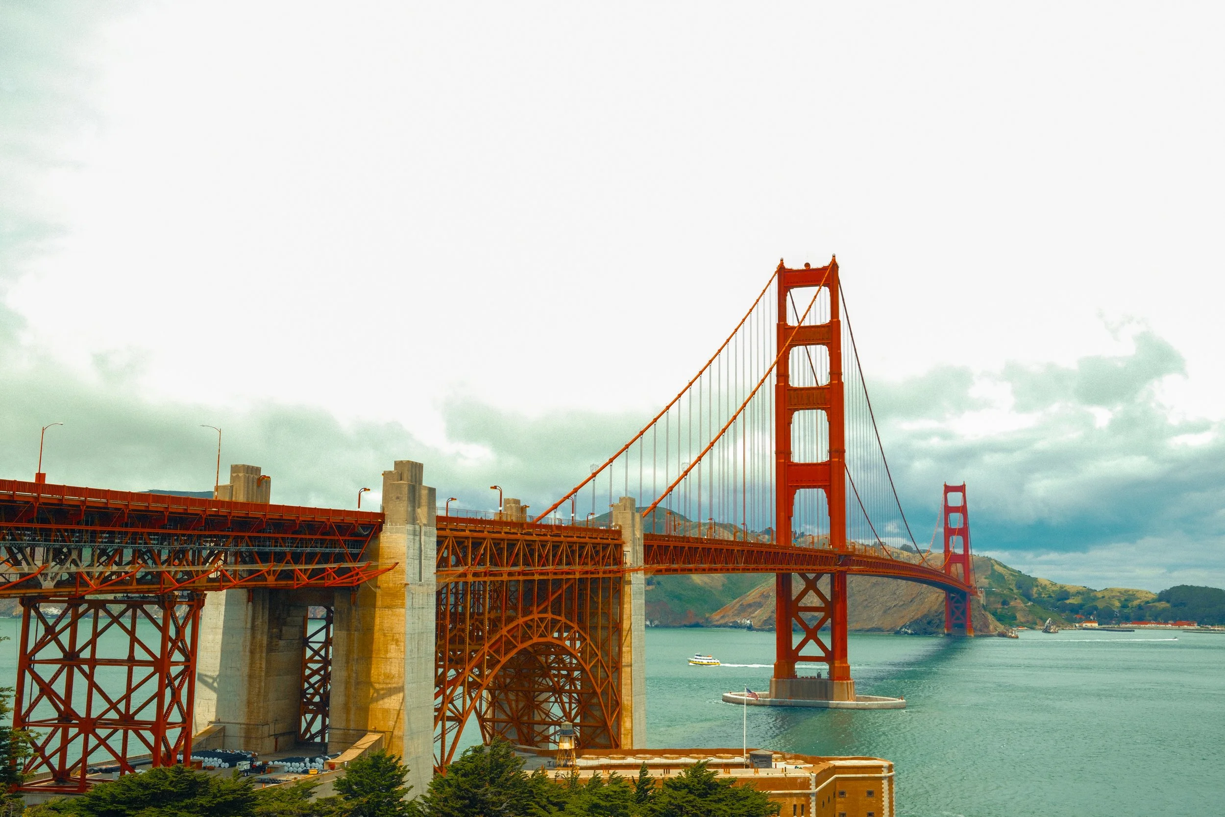 Golden Gate Bridge in San Francisco, California, with water and a boat underneath, and cloudy sky overhead.