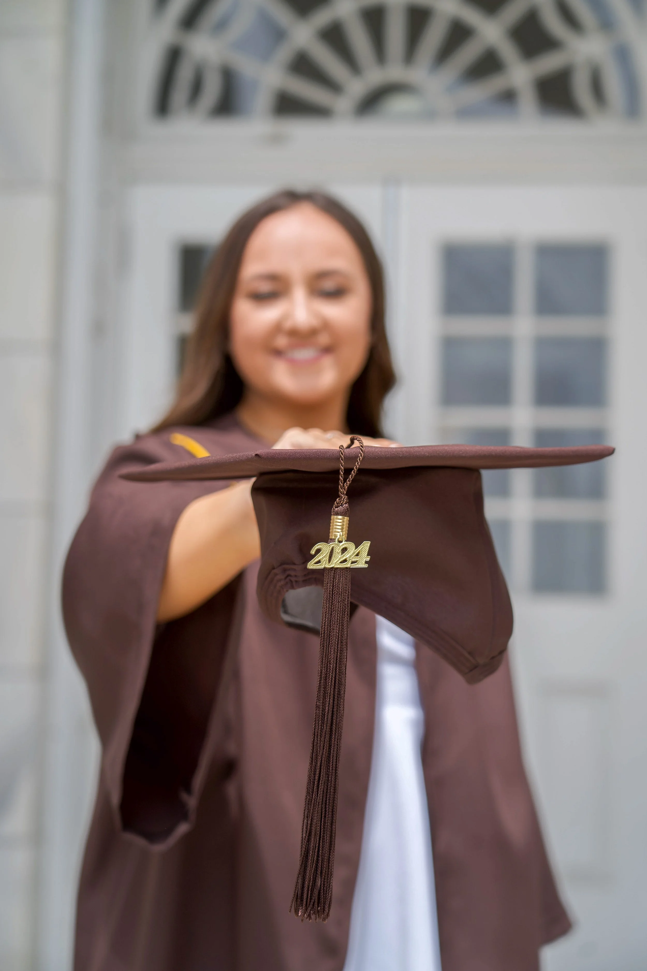 A young woman in a graduation gown holding a tassel with the year 2024 pendant