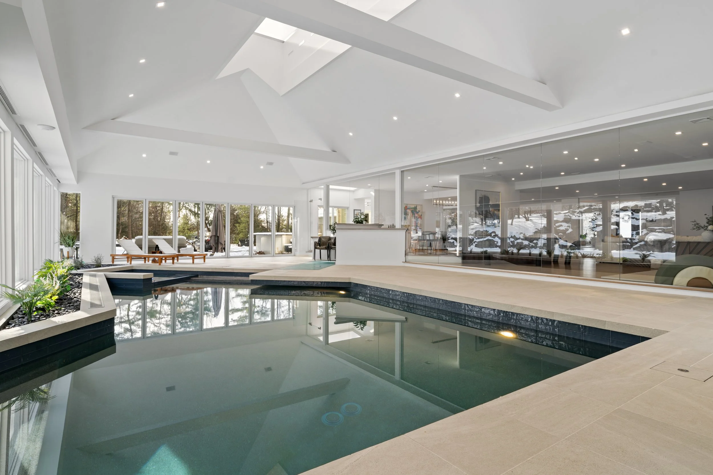 Indoor swimming pool area with large windows, lounge chairs, and a view of a snowy landscape outside.