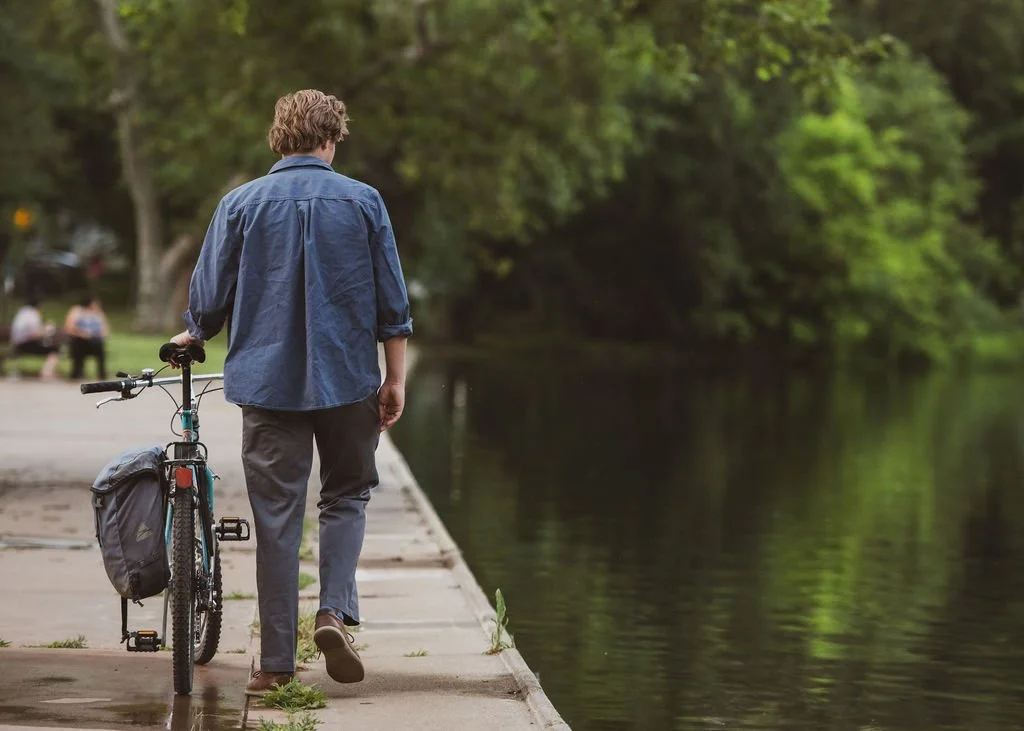 Addison Winslow walking with a bicycle along a tree-lined path in Chico.