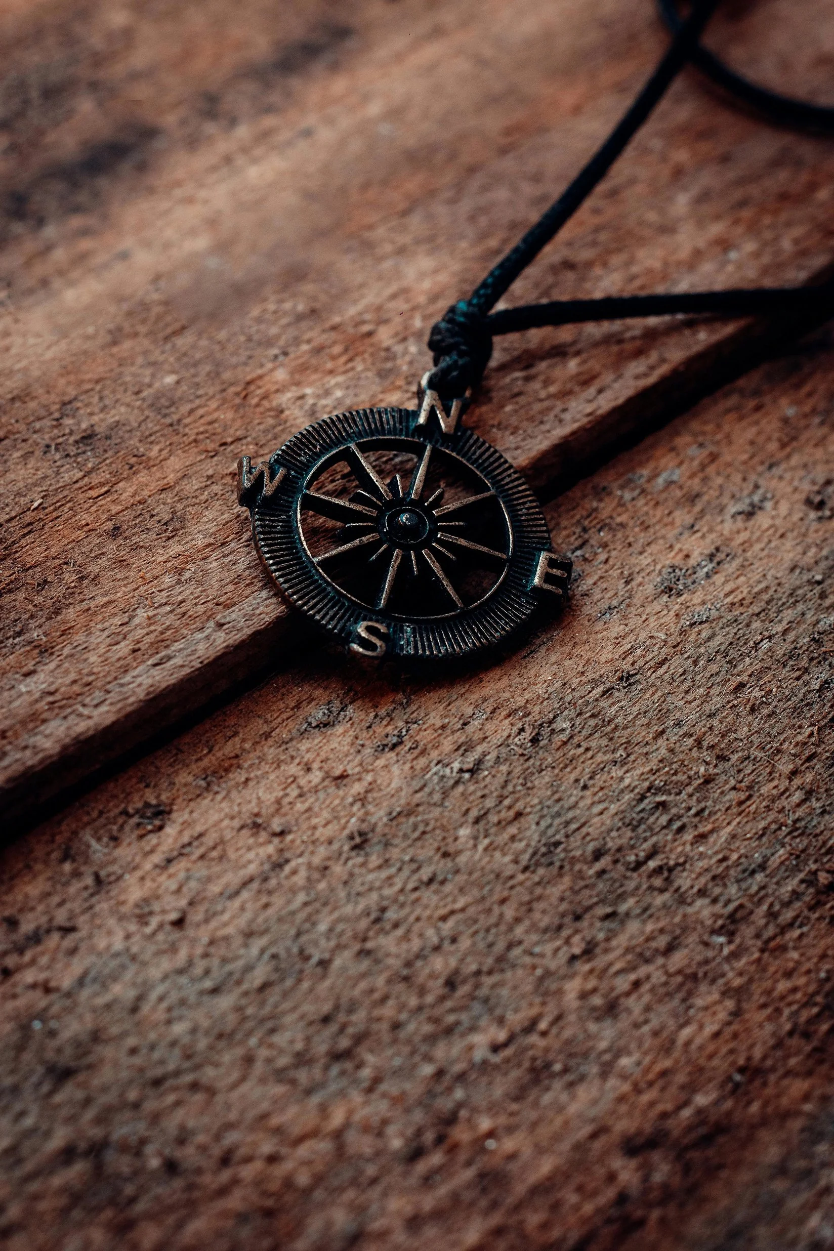 A necklace with a compass pendant resting on a textured wooden surface.