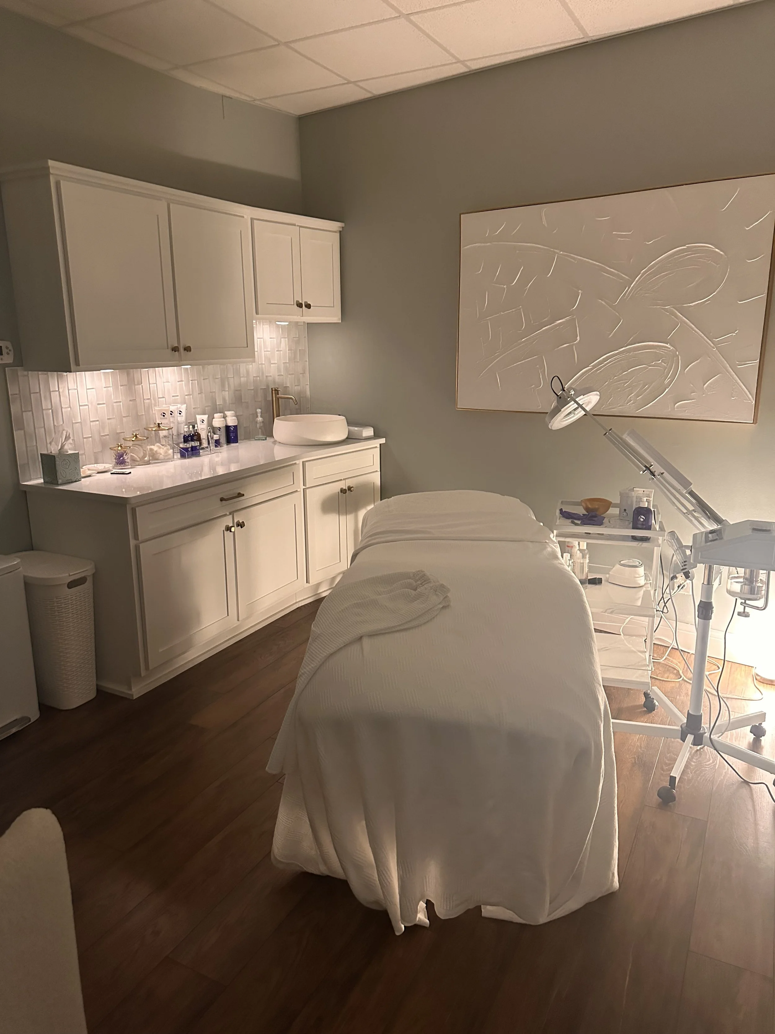 Medical treatment room with a massage bed, medical equipment, and a large abstract art on the wall.