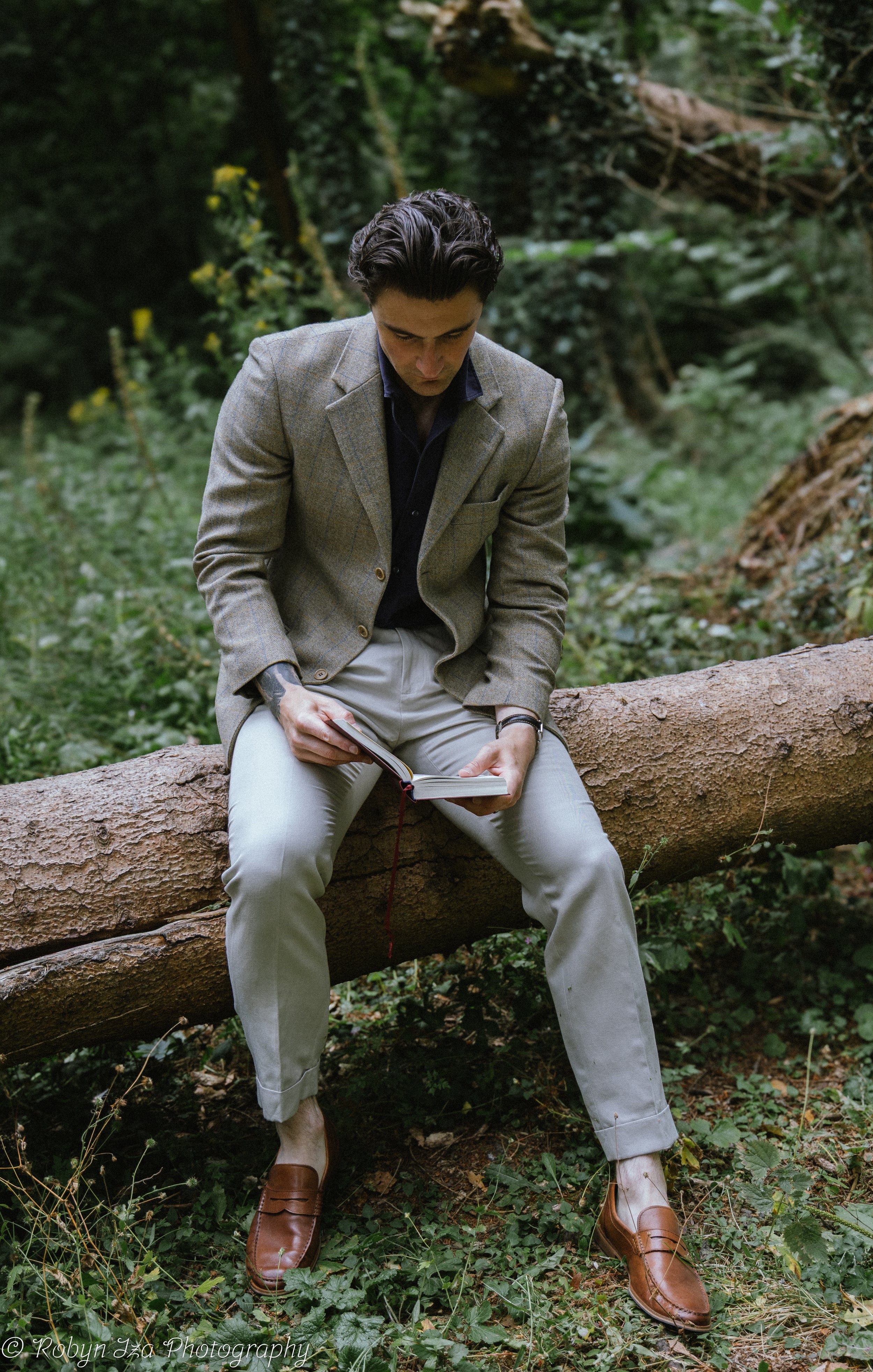 Man in woods sitting on a log reading a book