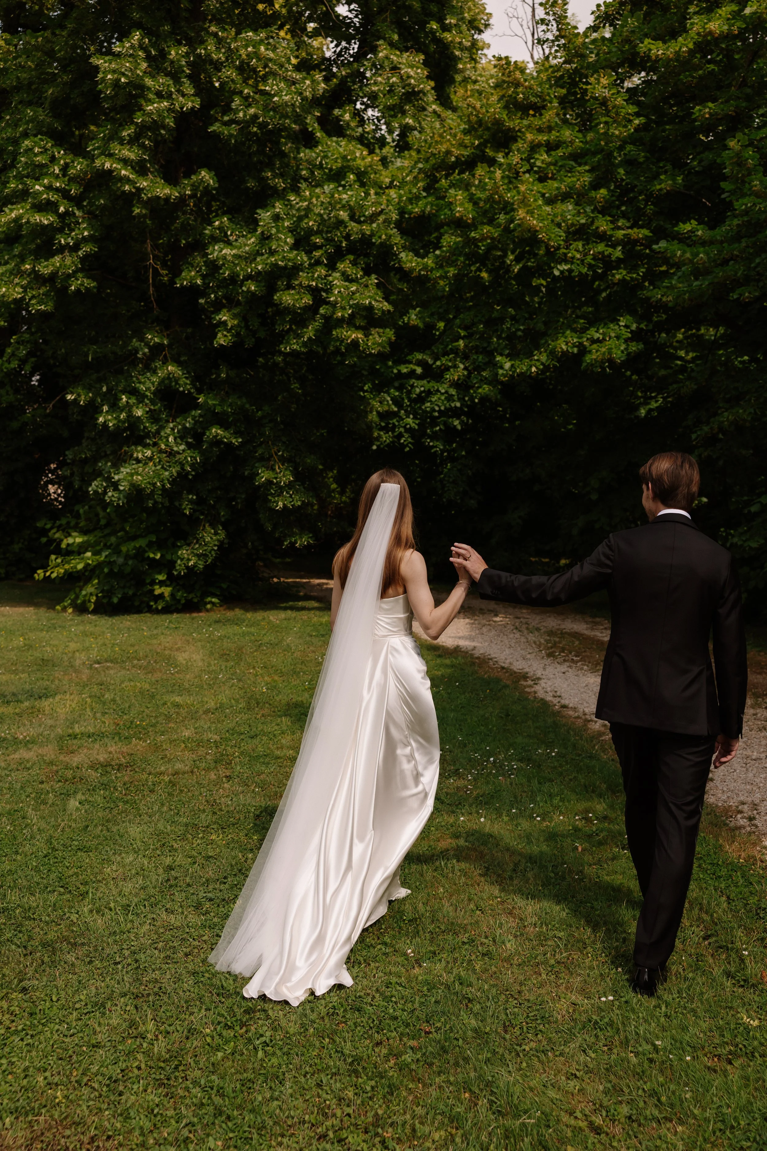 Black-tie wedding couple walking together after the ceremony, captured from behind with a refined and timeless aesthetic.