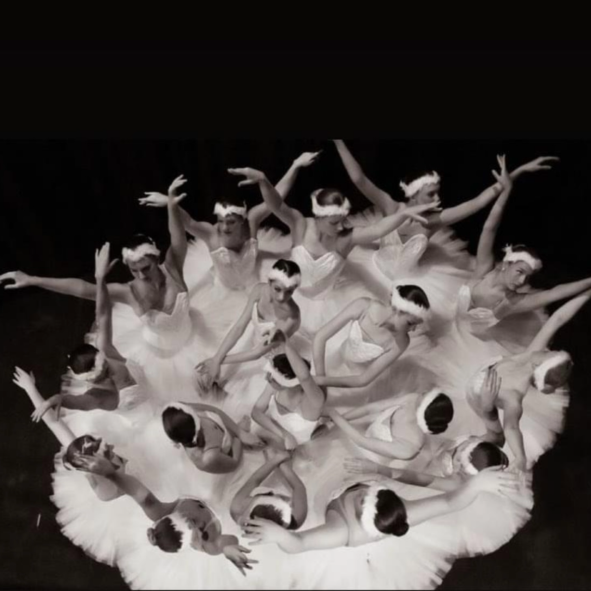 A group of ballerinas in white tutus and headbands, performing a dance on stage with their arms extended gracefully.