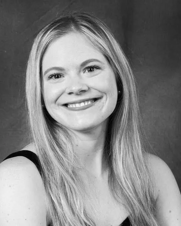 Black and white portrait of a smiling woman with long, straight hair, wearing a sleeveless top, against a plain background.