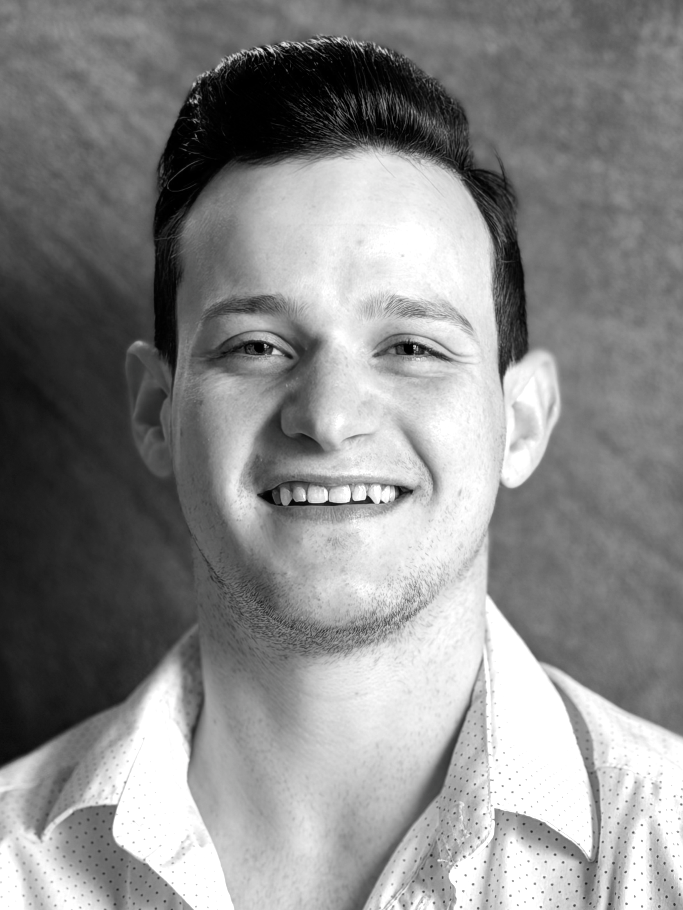 Black-and-white portrait of a smiling man with short styled hair, wearing a polka-dot shirt with an open collar.