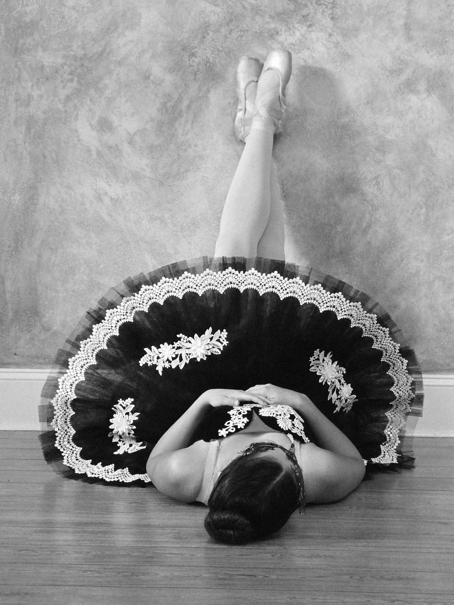 A person lying on the floor wearing a ballet costume with a large decorated tutu and ballet shoes.