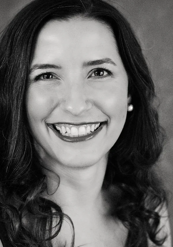 Black and white close-up portrait of a smiling woman with wavy hair, wearing pearl earrings.
