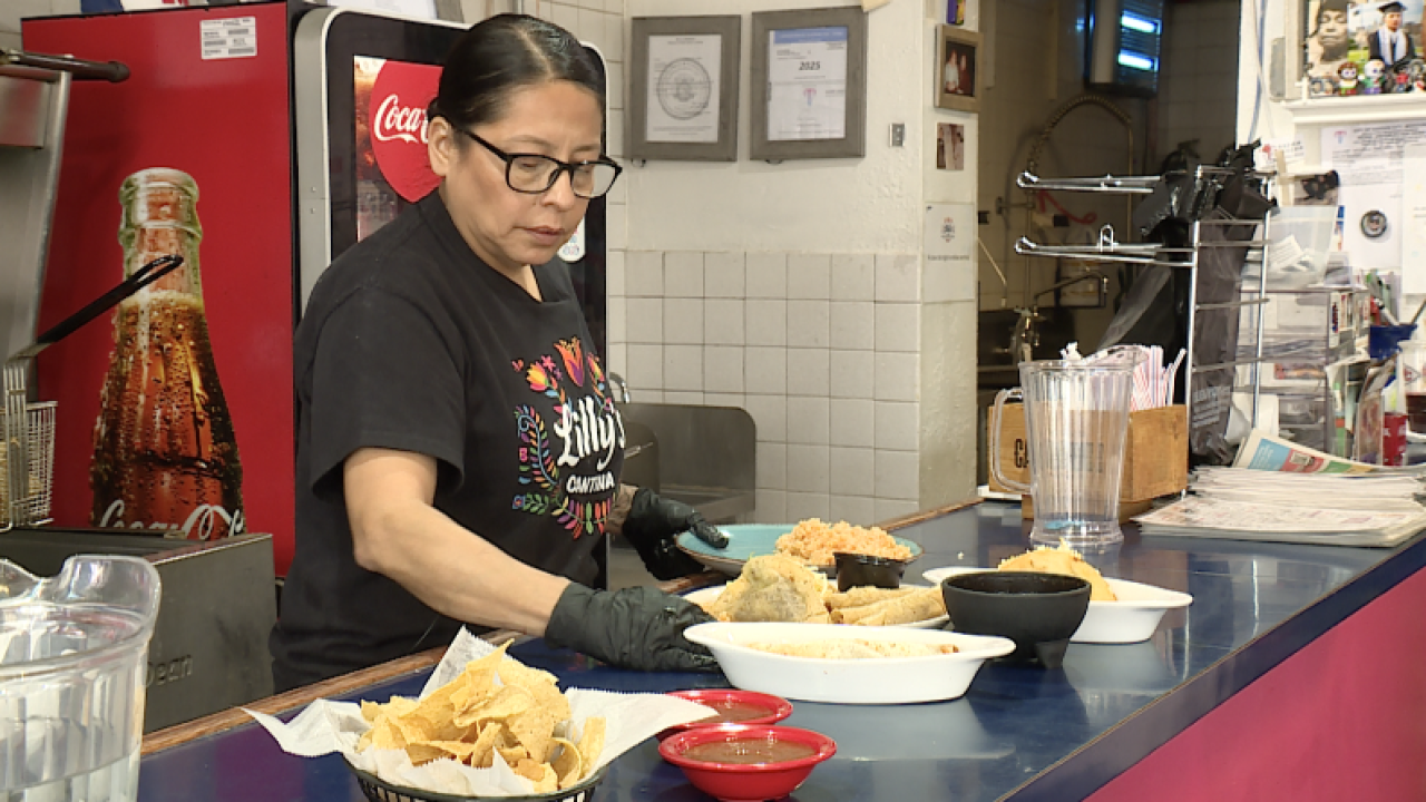 A woman with glasses wearing black gloves preparing food at a restaurant counter with various dishes and condiments.